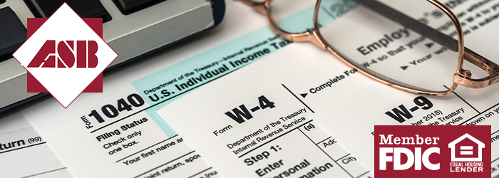 Stack of tax forms with reading glasses and edge of laptop on them