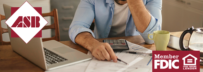 Man with his hand on his head sitting at the table with his laptop, financial documents, coffee, and calculator