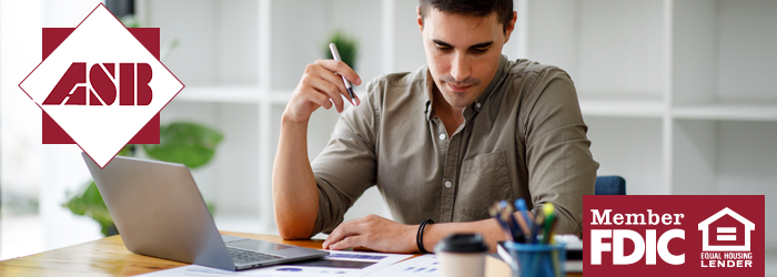 Young adult sitting at a desk with his laptop and some financial reports in front of him