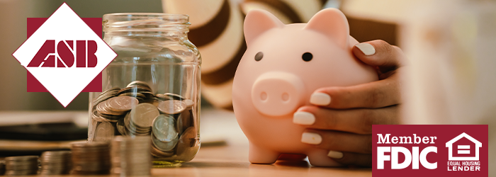 Woman's hand around a pink piggy bank with a clear jar of coins next to it