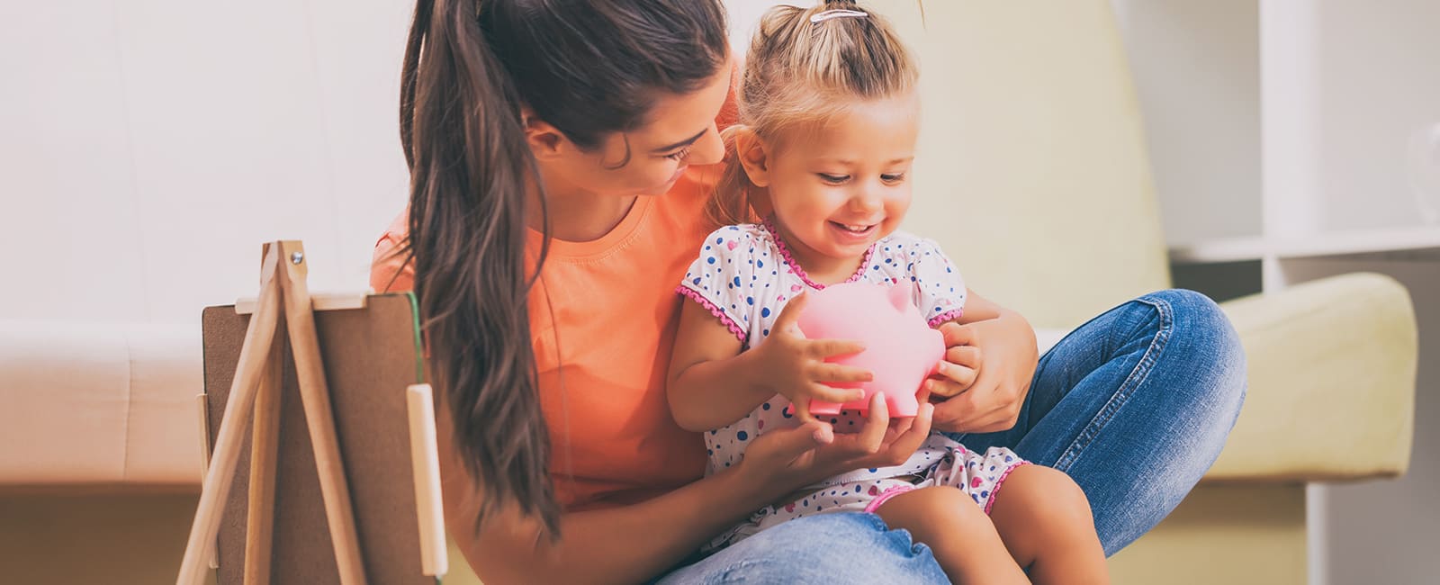 mom holding young daughter with piggy bank